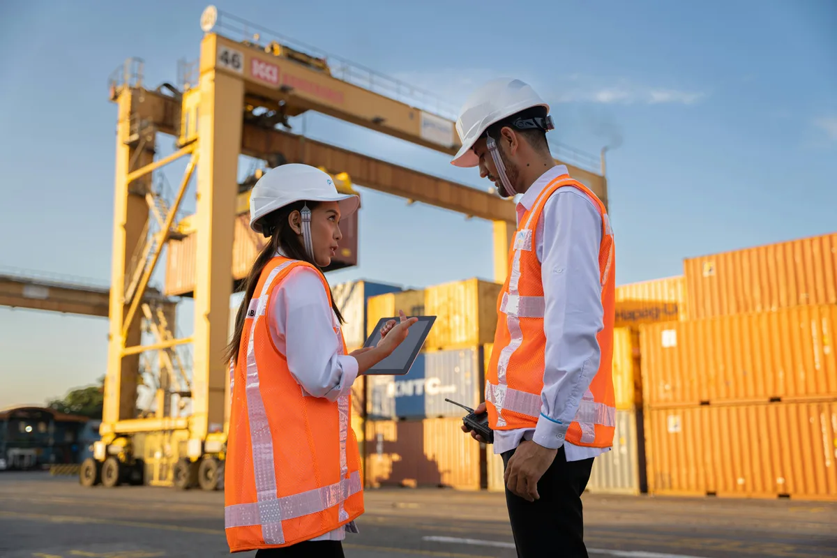 Two people in safety equipment reviewing a tablet on an industrial site